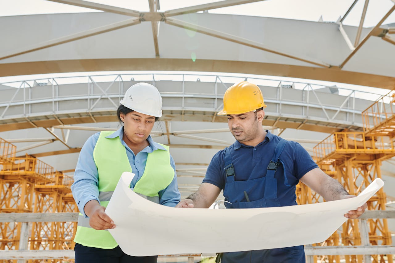 hero-img-01 Male and female engineers discussing blueprints at a construction site, promoting teamwork and planning.