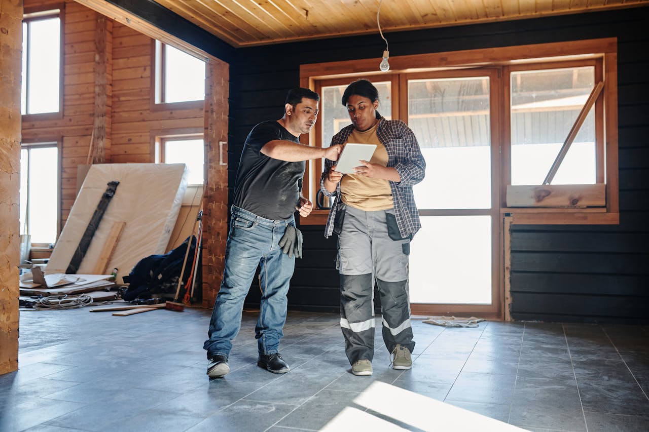 why-choose-us Two construction workers inside a house reviewing renovation plans on a digital tablet.